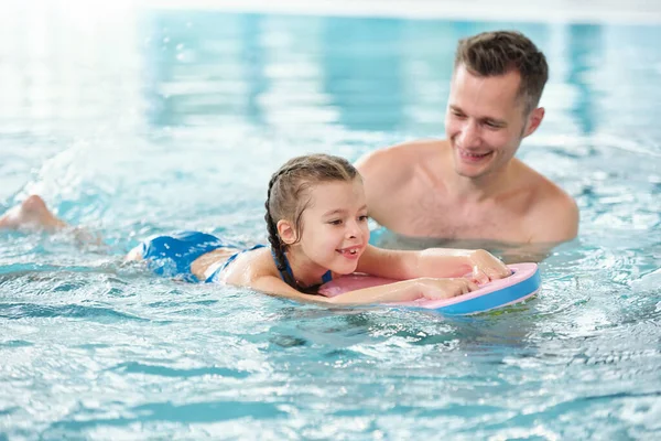 快乐的年轻父亲教他可爱的小女儿在游泳池里游泳 同时在温泉中心或避暑胜地度假 — 图库照片