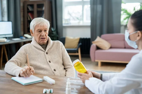 老年人穿着便服 看着坐在他面前的年轻女医生手里拿着药瓶 给他提建议 — 图库照片