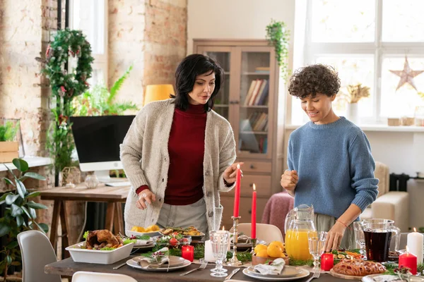 Two females discussing where to put this or that homemade food while standing by served table and getting ready for family xmas dinner