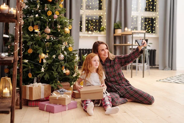 一个快乐的女人 一个穿着睡衣的可爱的小女孩 在自家客厅中央的一棵装饰过的圣诞树下自作主张 — 图库照片