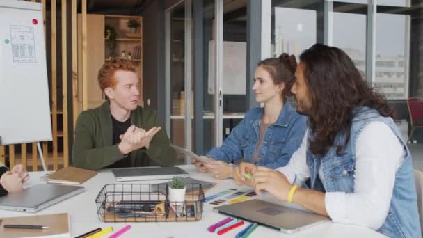 会議室でテーブルの周りに座って プロジェクトのアイデアを議論する陽気な若いスタートアップ企業の従業員のPanショット — ストック動画