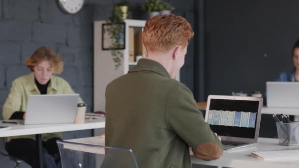 オフィスのデスクに座って新しいアプリインターフェーステンプレートを見ている若い男性UiデザイナーのPanリアビュー — ストック動画