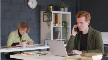 Ofiste oturan ve cep telefonuyla konuşurken dizüstü bilgisayarda çalışan meşgul genç işadamlarının PAN 'ı.