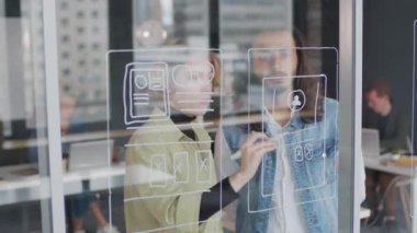 Genç bayan UI tasarımcısının ofisteki cam duvar ya da pencereye arayüz fikirleri çizerken ve erkek meslektaşımla konuşurken PAN çekimi