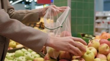 Orta bölüm yavaş çekimde, tanınmayan kadın ellerinin taze organik elmaları seçerek büyük bir süpermarkette onları eko-torbaya koyması.