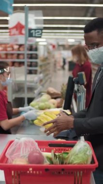 Süpermarketten koruyucu maske takarak taze gıda ürünleri alan Afro-Amerikan iş adamlarının dikey görüntüsü.