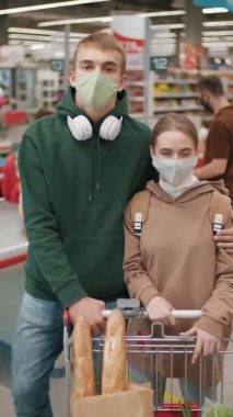 Süpermarkette alışveriş yaptıktan sonra maske takan ve maske takan mutlu çiftin orta boy dikey portresi.