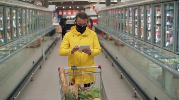 Közepes Lassított Felvételű Férfi Áll Szupermarket Folyosóján Bevásárlókocsival Nézi Bevásárlólistát — Stock videók
