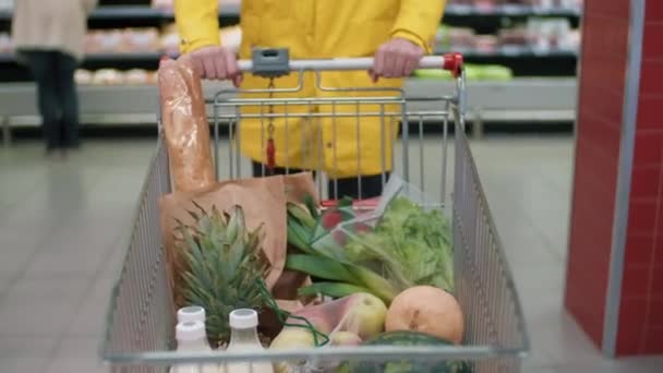 身着鲜亮黄色外套的男子载着装有健康食品的购物车沿着超级市场行走的中间镜头 — 图库视频影像