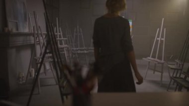 Karanlık sanatçılar stüdyosunun odasına giren tanınmamış zarif kadın ressamın, resim sehpasındaki soyut tuvali bitirdiği arka plan görüntüleri.