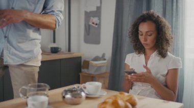 Kafkasyalı genç bir kadının kahvaltıda akıllı telefon kullanırken, tartışırken ve kocasıyla kavga ederken cep telefonunu birbirlerine bağırarak almaya çalışırken orta yavaş çekimleri.