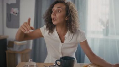 Mutfak masasında oturmuş umutsuzluk içinde ellerini dağıtan yorgun ve mutsuz bir kadının orta yavaş çekimi.