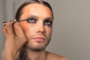 Sahne performansı için hazırlarken sakallı bir kadına rimel süren tanınmamış bir adam.