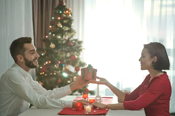 幸福的年轻夫妇坐在桌旁 点燃蜡烛 牵着手交换圣诞礼物 — 图库照片