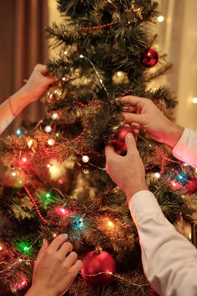 女性の手はクリスマスライトを調整しながら 木の上にクリスマスの泡をぶら下げ認識できない男のクローズアップ — ストック写真