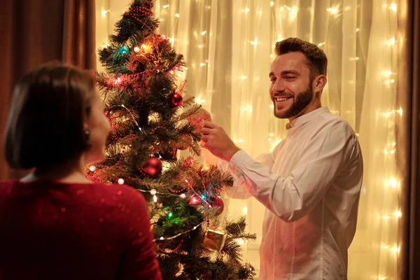彼らはお祝いの準備中にガールフレンドとクリスマスツリーを飾る白いシャツの髭の男を笑顔 — ストック写真