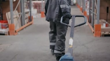 İnşaatta çalışan işçilerin forklift taşıdığı arka plan görüntüleri. Bu sırada birkaç işçi, büyük bir depoda palet rafları boyunca ellerinde ıvır zıvırla yürüyorlar.