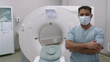 Hastanede tomografi odasında kollarını kavuşturup kameraya bakan yüzü maskeli Arap erkek doktorların portresi.