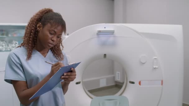 在放射科病房剪贴板上书写的笔刷中的黑人女性Ct技术的Pan照片 然后看着相机 — 图库视频影像
