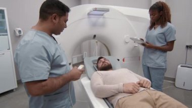 Arap erkek radyologun ameliyat sonrası tomografisini çekerken önlüklü kadın teknisyen olarak tabletin yanında durup yazarken.