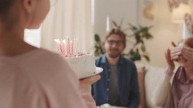 Küçük bir kızın güzel bir doğum günü pastasıyla odaya girip mumları yakarak tatilde kapalı gözlerle güzel büyükannesine verdiği yavaş çekim.
