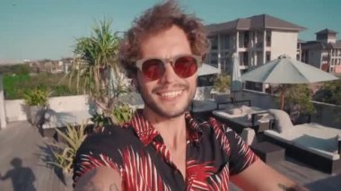 Yakışıklı adamın el sallayarak akıllı telefona merhaba deyip egzotik bir ülkede tatilde video görüşmesi yapması.