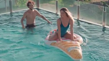Yüzme havuzunda dondurmalı su yatağı süren ve onu iten genç ve havalı bir çiftin yüksek açılı görüntüsü.