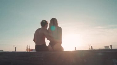 Yaz çifti, lüks bir tatil köyünde havuzun kenarında oturup güneşin batışını izlerken arka plan görüntüsü.