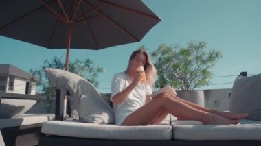 Alçak açılı, mükemmel vücutlu çekici bir kadının güneş altında uzanmış içeceğini yudumlarken ve kitap okurken.