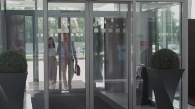 Orta yaşlı bir kadın ve orta yaşlı bir adamın araba galerisine sürgülü cam kapılardan girerken çekilmiş bir fotoğrafı.