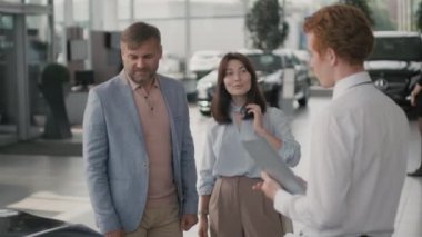 Orta yaşlı bir adamın arabanın kaputuna dokunduğunu ve galeride araba satıcısıyla konuştuğunu, sonra da onunla el sıkıştığını görmek. Kocasının yanında duran ve gülümseyen neşeli genç kadın.