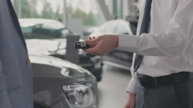 Resmi giyinmiş, tanınmayan bir satıcının resmi araba anahtarlarını erkek müşteriye teslim etmesi ve anlaşma bittikten sonra el sıkışması.