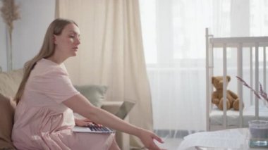 Genç hamile bir kadının bilgisayarında yazı yazarken ve evrak işleriyle uğraşırken orta yavaş çekimde çekilmiş görüntüleri.