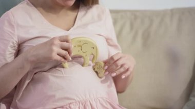 Orta bölüm yavaş çekim. Pembe elbiseli, hamile bir kadın karnında fili oynuyor. Evdeki kanepede dinleniyor.