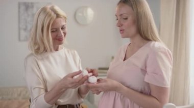 Yetişkin anne ve hamile kızın orta yavaş bir şekilde el ele tutuşan ve gülümseyen küçük popolardan bahsettiği bir yer.