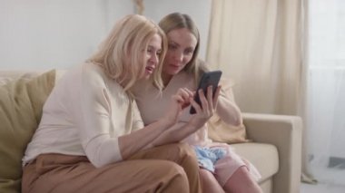 Müstakbel bebeğinin ultrason fotoğrafını, oturma odasındaki koltukta oturan sürpriz anneye gösteren mutlu ve hamile kadının orta yavaş çekim görüntüleri.