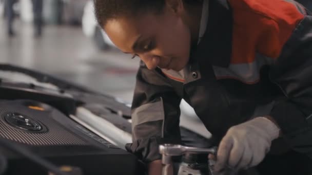 穿着制服戴手套的黑人女汽车修理工手握倾斜镜头 用工具在车库里修理客户的汽车 — 图库视频影像