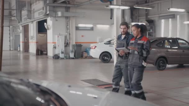 Weitwinkelaufnahme Einer Schwarzen Automechanikerin Mit Tablet Und Ihres Bärtigen Männlichen — Stockvideo