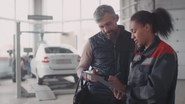 Siyah Kadın Otomobil Tamircisinin Pano Tutarken Erkek Müşteriyle Konuşurken Orta — Stok video