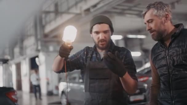 Handheld Schot Van Bebaarde Mannelijke Automonteur Met Draagbare Werklicht Praten — Stockvideo