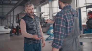 Yavaş çekimde sakallı erkek müşterinin otomobil tamirhanesinde arabasının anahtarlarını teslim ederken.