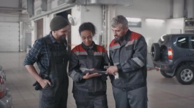 Üniformalı kadın ve erkek oto tamircilerinin otoparkta konuşmalarının ve tablet kullanmalarının portresi.