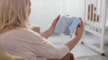 Genç ve mutlu, hamile bir kadının, oturma odasındaki kanepede oturup mavi yeni doğan bebeğe bakıp gülümsemesi ve sonra da kameraya bakması.