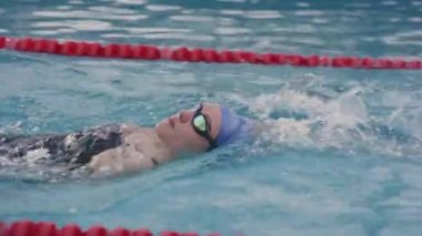 Kadın yüzücünün yavaş çekimde sırtüstü bilardoda sürünürken, antrenmanı bitirdikten sonra gözlüğünü çıkarırken.