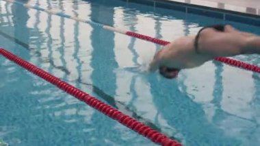 Erkek profesyonel yüzücünün kasketli ve şortlu yavaş çekim şeritli kapalı havuza dalışları.