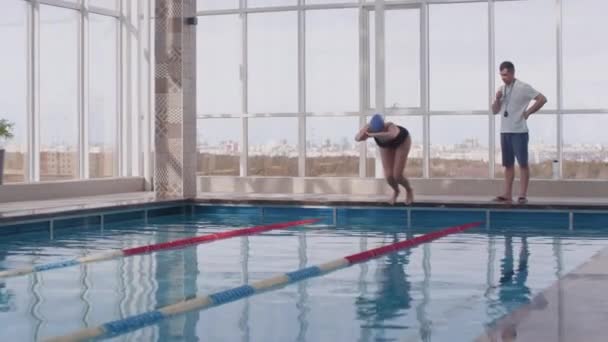 男子教练慢吞吞地看着女游泳运动员在练习过程中跳入游泳池 — 图库视频影像