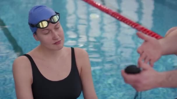 追踪无法辨认的男教练谈话的镜头 并向在室内游泳池练习的女游泳运动员展示秒表 — 图库视频影像