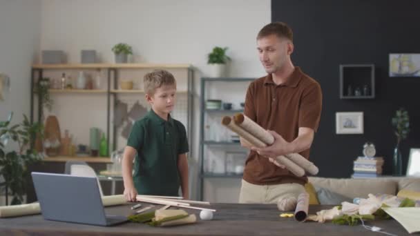 Střední záběry radostného muže a jeho malého syna v obývacím pokoji, jak připravují materiály pro domácí draka, jak spolu tráví čas