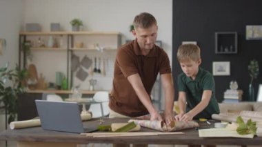 Baba ve oğulun ev yapımı uçan kağıt uçurtma yapıp dizüstü bilgisayarda video izlediği orta ölçekli yavaş çekim görüntüleri.