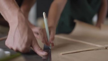 El yapımı kağıt uçurtma çizen tanınmayan bir adamla küçük çocuğun orta bölüm yavaş çekim çekimi. Çizimler çizmek için kalem ve cetvel kullanıyorlar.